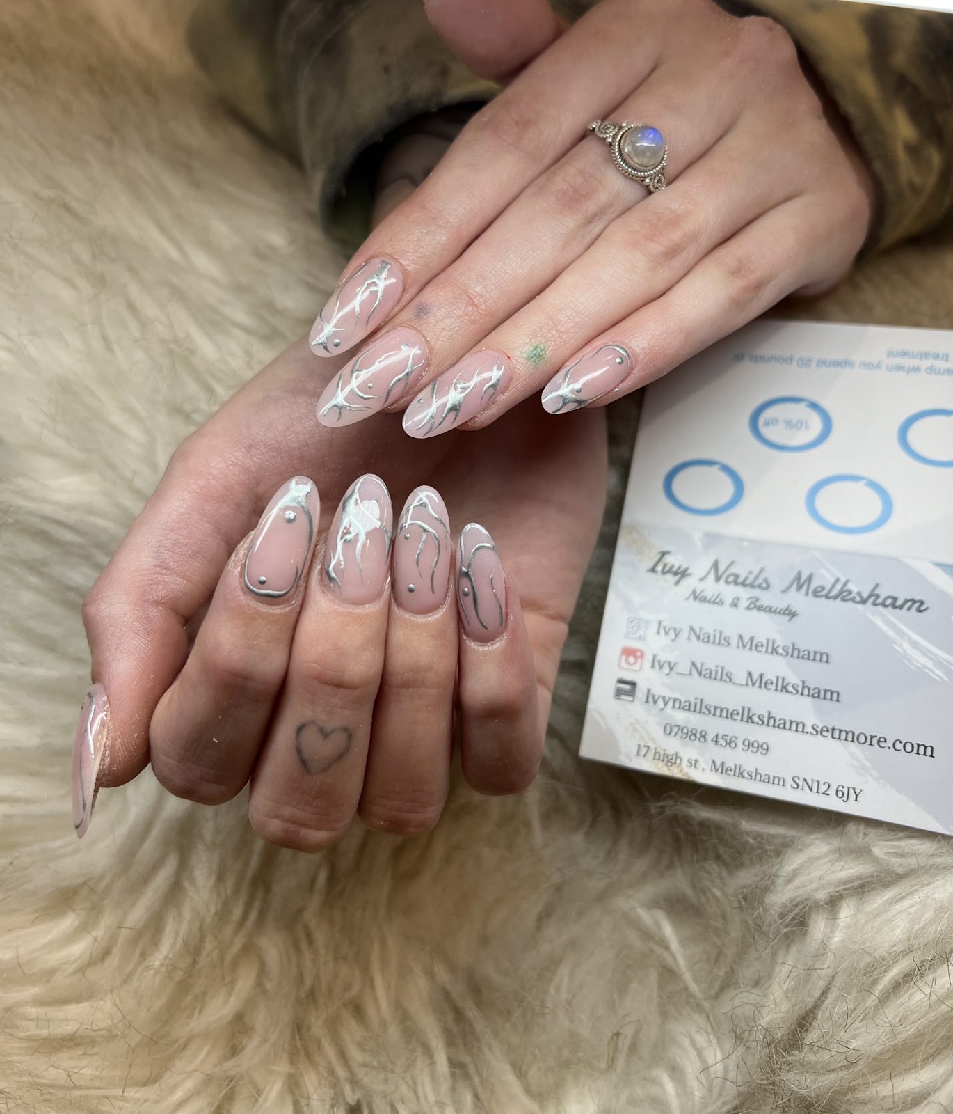 Long nude almond nails with silver chrome line art, resting on a fur cushion