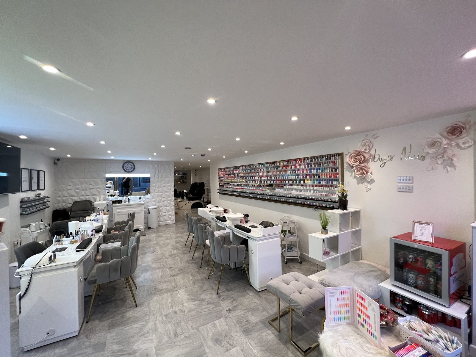 Inside Ivy’s Nail Lounge: rows of white nail desks, a wall of polish colours and pink floral wall art