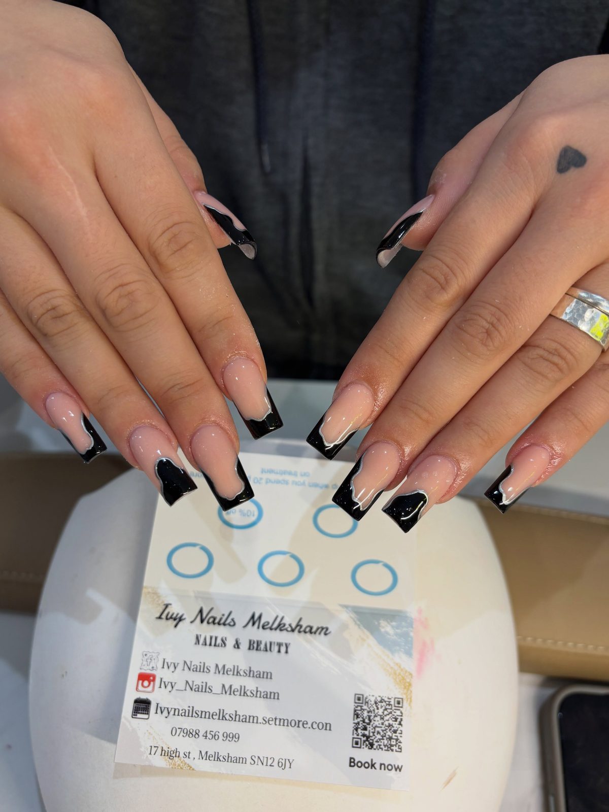 Nude almond nails with black French tips beside an Ivy Nails business card
